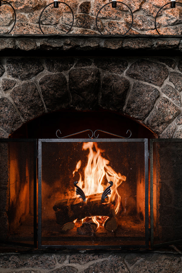 Stone fireplace with burning logs and metal screen