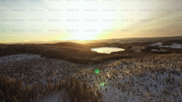Vintersolnedgång över frusen sjö och snötäckt skog i Gunnarsbyn, Sverige