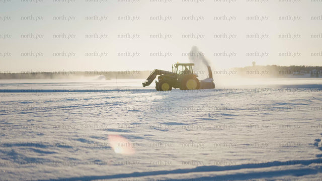 Tractor clearing snow on frozen lake in Luleå during golden hour
