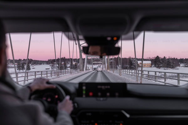 Car driving across snowy bridge at dusk