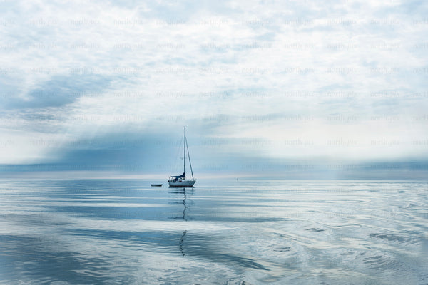 Sailboat anchored on calm sea under cloudy sky