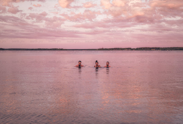 Three people swimming in lake at sunset