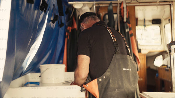 Fisherman cleans fish on boat while wearing orange gloves and overalls