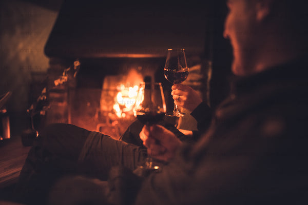 Two people holding wine by a fireplace at night