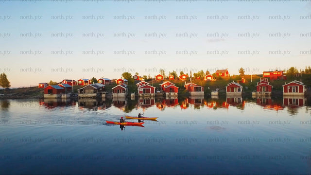 Kayaking in Luleå archipelago at sunset with red cabins: A summer drone view
