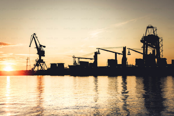 Harbor cranes loading cargo at sunset over water