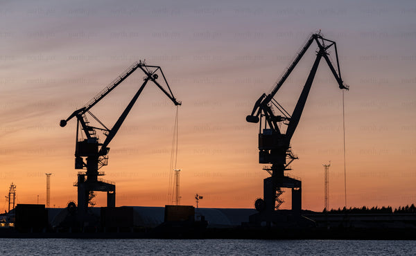 Two harbor cranes silhouetted against sunset sky at port of Luleå