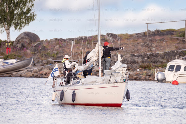 Sailboat with crew near rocky shore in daylight