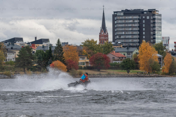 Person on jet ski near waterfront town in autumn