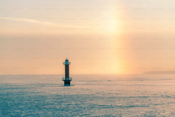 Lighthouse on frozen sea at sunrise