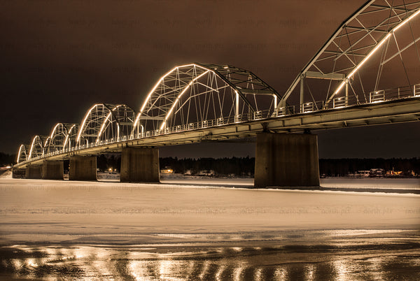 Illuminated arched bridge over frozen river at night