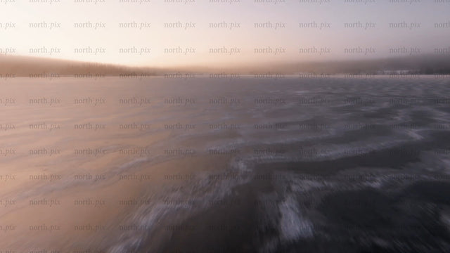 Low-level aerial drone footage over frozen lake at sunset in arvidsjaur