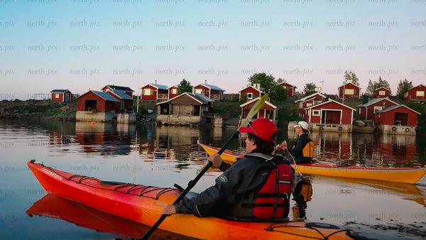 Kayaking past red cabins in the Luleå archipelago at twilight