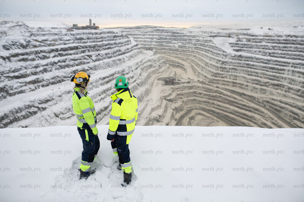 Two workers overlooking snowy open pit mine in winter