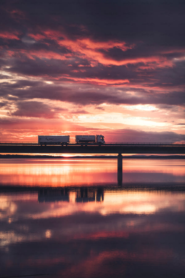 Truck crossing bridge at sunset with water reflection