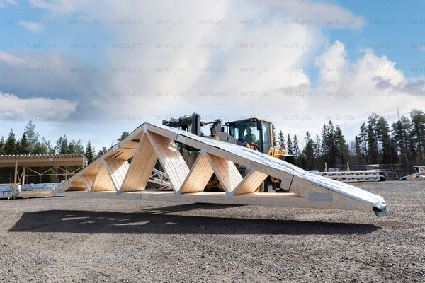 Wooden roof truss lifted by loader in construction yard