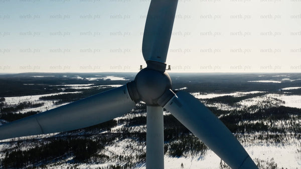 Wind turbine rotating against blue sky in snowy winter landscape
