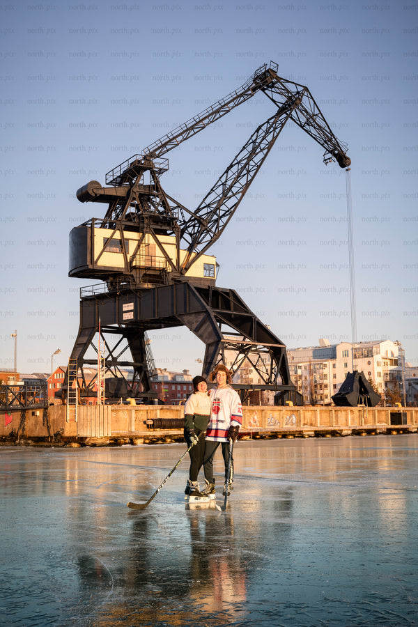 Two people playing ice hockey by harbor crane at sunset