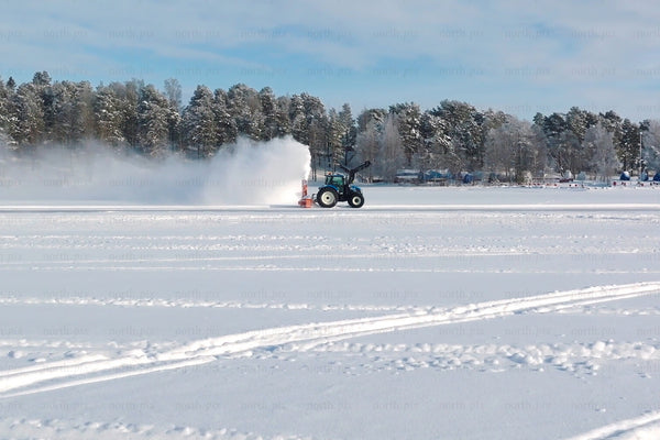 Winter snow field with tractor clearing snow on frozen lake near Luleå city center