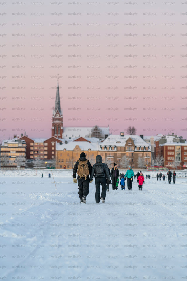 Two people walking on ice road toward snowy city