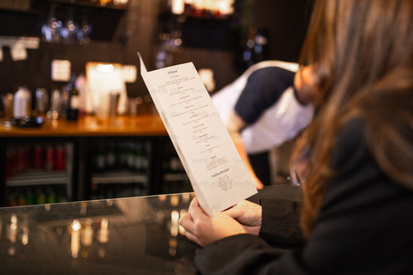 Person reading a menu at a bar counter in evening
