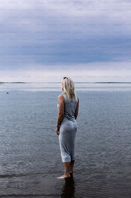 Woman standing on shoreline looking toward horizon, daytime