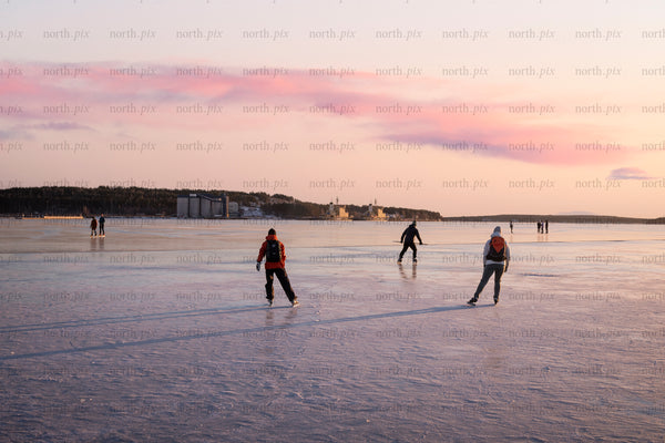 People ice skating on frozen sea at sunset
