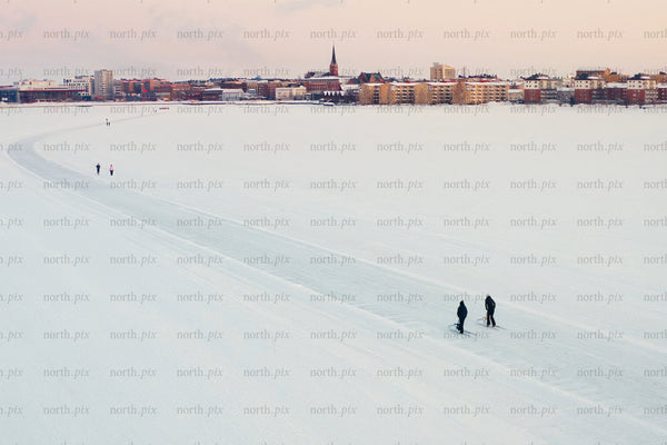 Snowy lake foreground with city center skyline of Luleå during winter calm soft sunset view