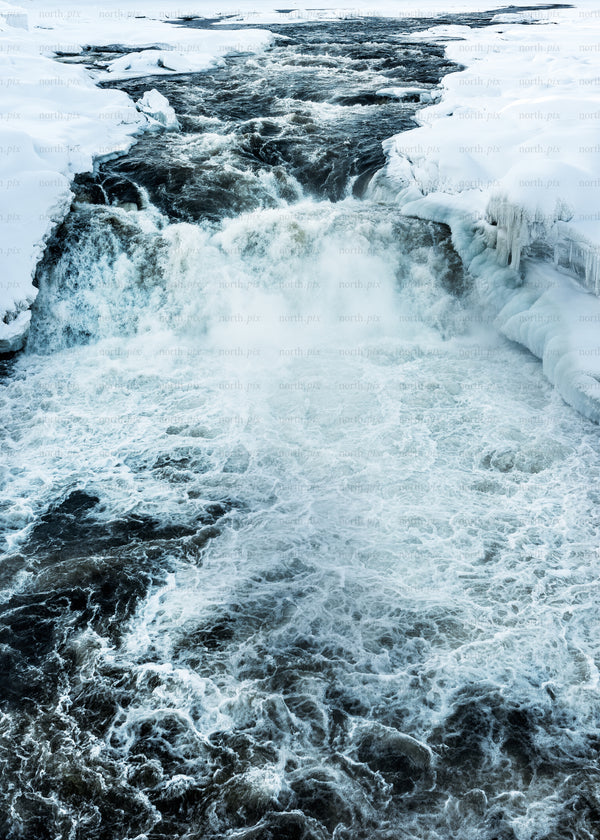 Icy waterfall and river flowing through snow-covered banks