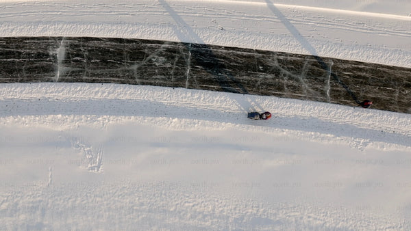 Aerial view of person pulling sled on frozen river in Luleå, on a sunny winter day