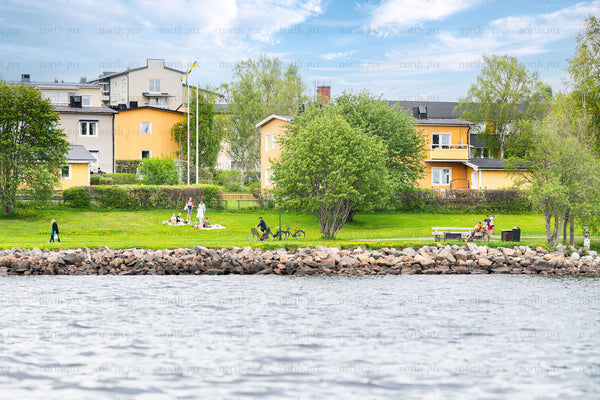 People in coastal park with yellow houses, summer day