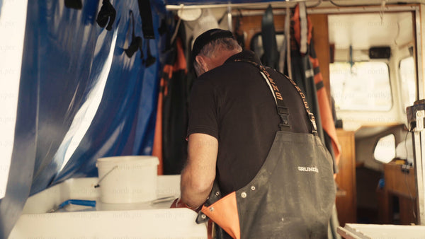 Fisherman cleans fish on boat while wearing orange gloves and overalls