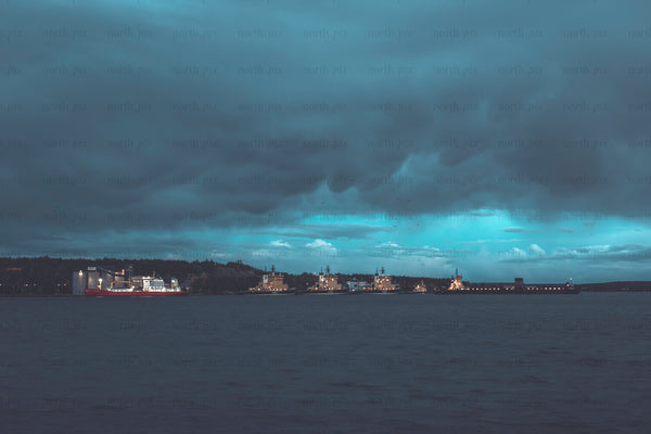Cargo ships moored at harbor under heavy clouds