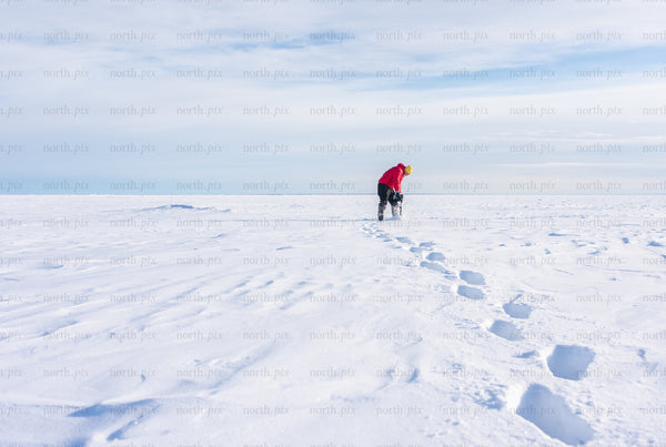 Person drilling ice on frozen lake at midday