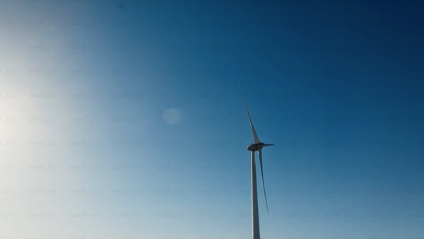 Wind turbine rotating against blue sky with sun, low angle view in winter