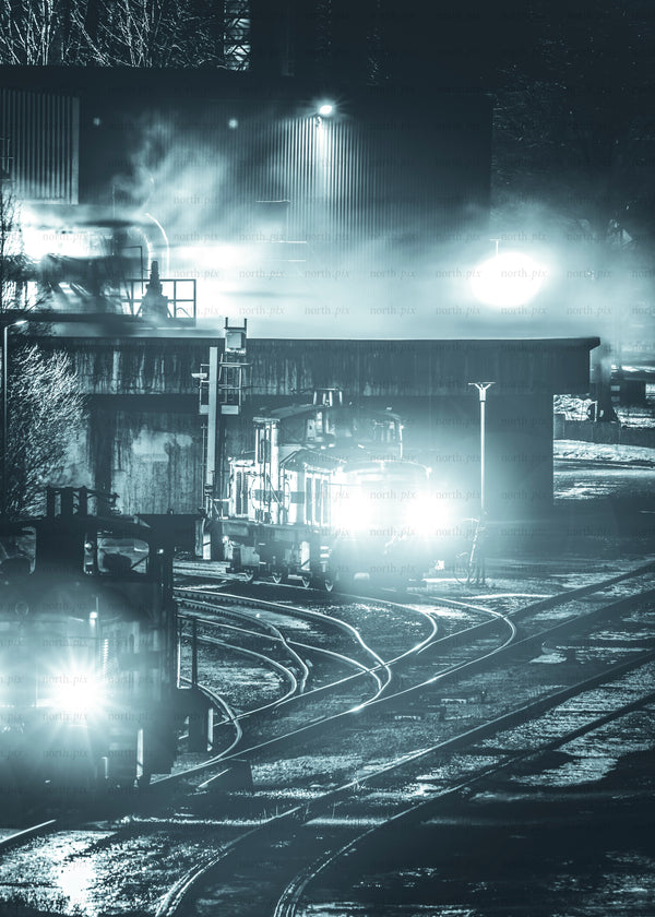 Locomotives in rail yard at night with headlights