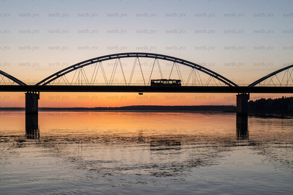 Tram crossing arch bridge over river at sunset