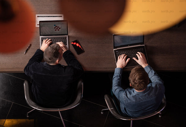 Overhead view of two men working on laptops