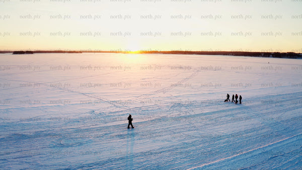 Friends enjoy a winter sunset walk on a frozen lake in Luleå