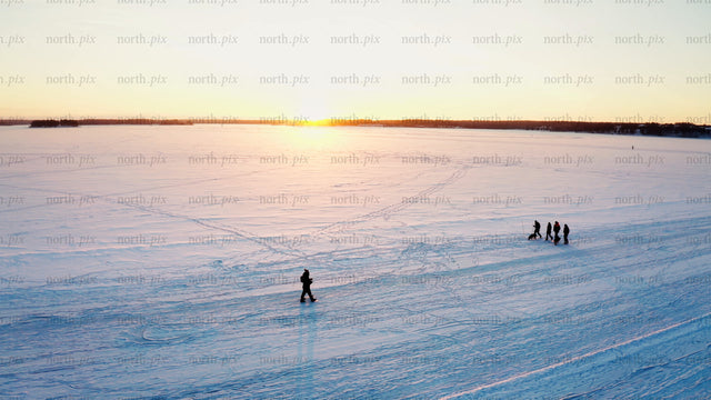 Friends enjoy a winter sunset walk on a frozen lake in Luleå