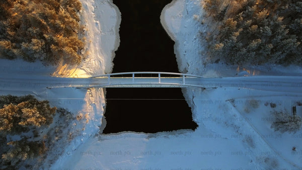 Winter landscape: Aerial view of bridge over frozen river at sunrise in Gunnarsbyn