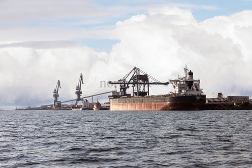 Lastfartyg förtöjt vid industrihamn med kranar