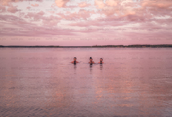Three people swimming in lake at sunset
