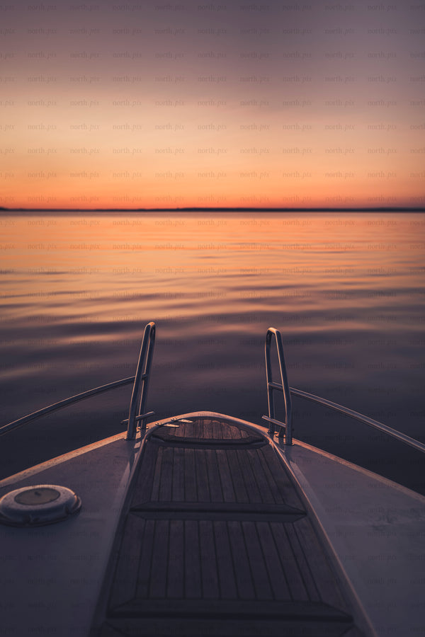 Bow of boat facing calm water at sunset