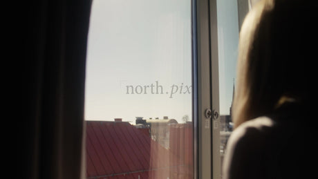 Woman Looking Out Hotel Window at Sunny Cityscape in Lulea, Sweden