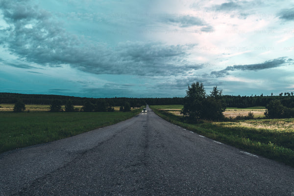 Road through countryside at dusk with car headlights