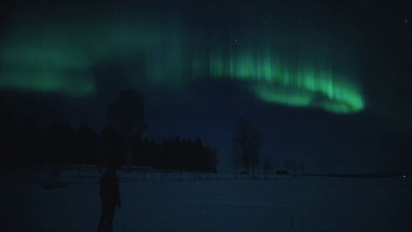 Person walking on a frozen lake under northern lights