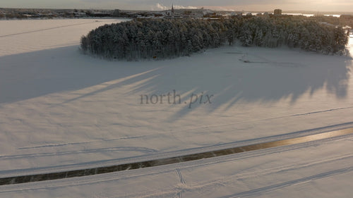 Vintersolnedgång över snötäckta Luleå, Sverige: Flygfoto från drönaren av frusen flod och isig väg