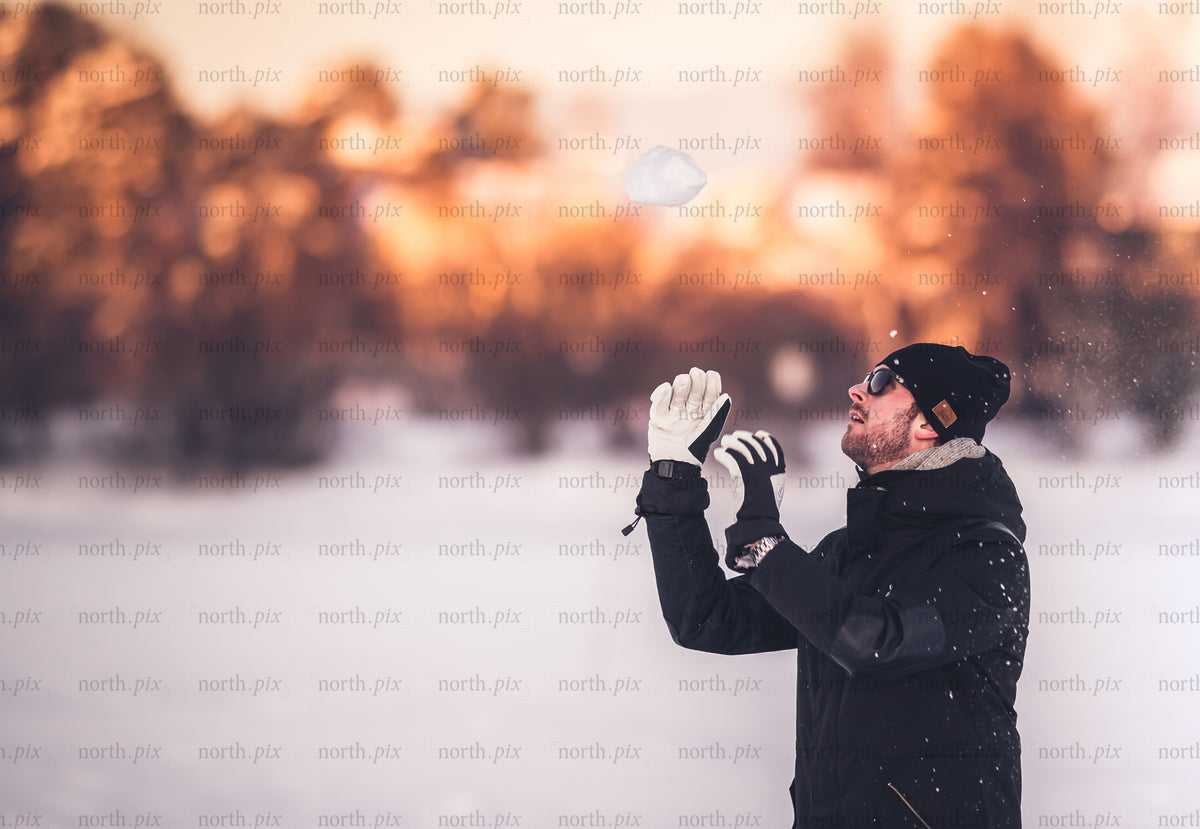 Man tossing snow in winter field at sunset