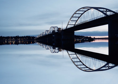 Bro reflekterad under blå timmens kväll över lugna vatten i Luleå, Sverige